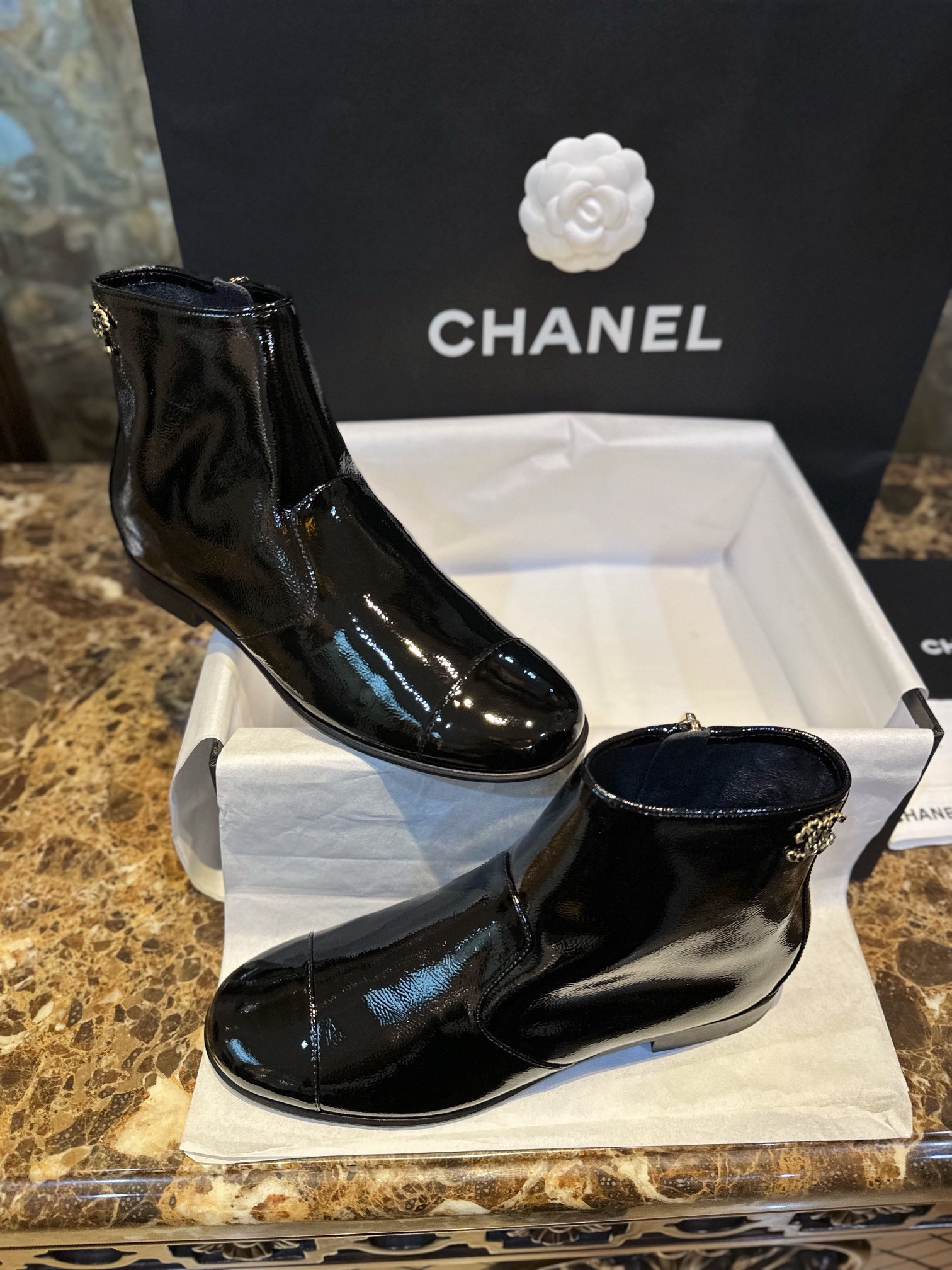 Chanel 23a Crinkled Patent Leather Chelsea Boots: A pair of understated yet exquisitely crafted ankle boots. Featuring sleek black patent leather with subtle gloss, minimalist design with only a brand logo decoration on the vamp. The interior is lined wit