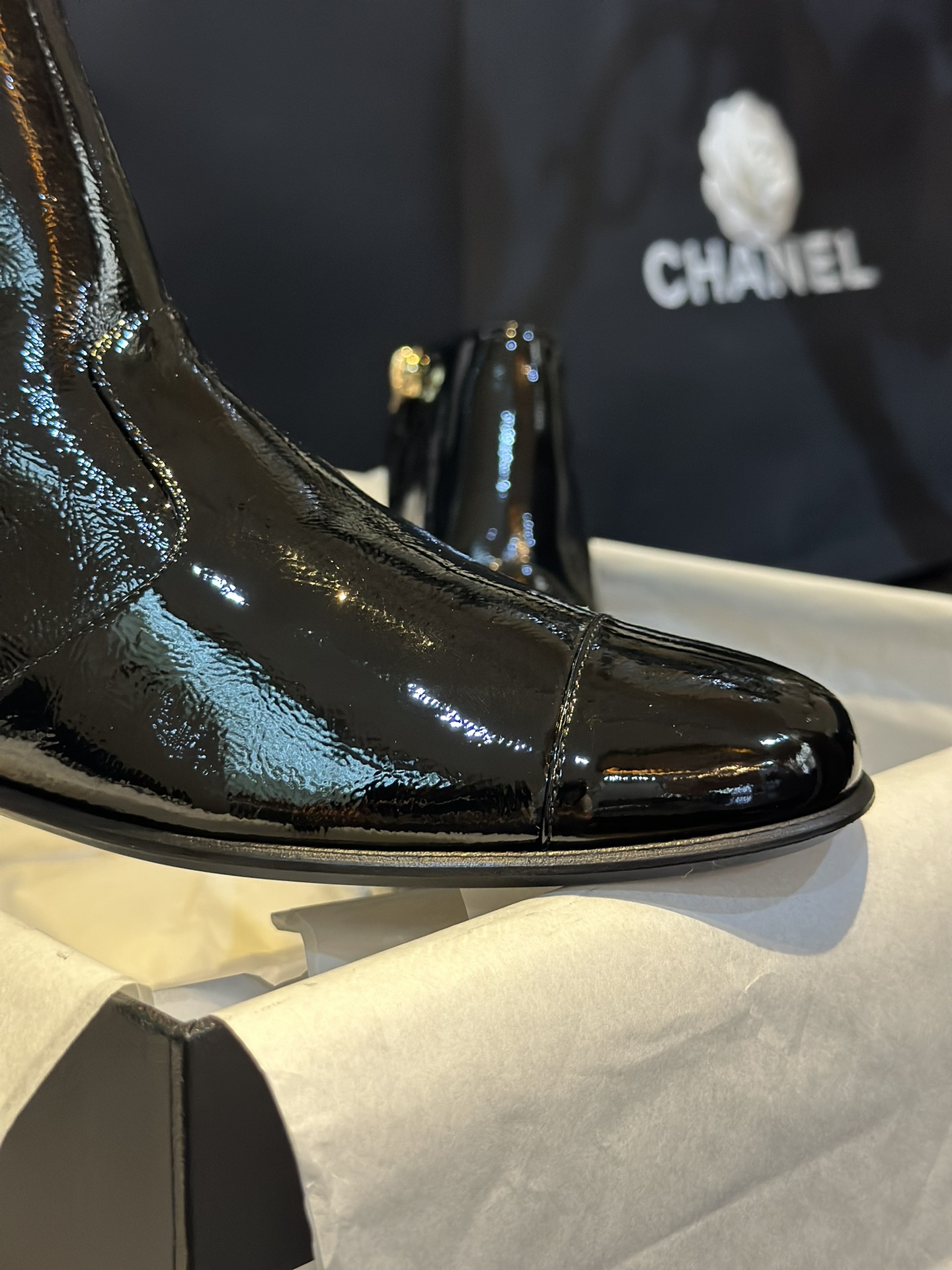 Chanel 23a Crinkled Patent Leather Chelsea Boots: A pair of understated yet exquisitely crafted ankle boots. Featuring sleek black patent leather with subtle gloss, minimalist design with only a brand logo decoration on the vamp. The interior is lined wit