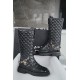 Chanel  23b  Chain Long Martin Boots: Crafted from black oil leather and black patent leather, with a leather combination sole. Classic diamond-pattern stitching and chain elements intertwine on the vamp