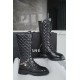 Chanel  23b  Chain Long Martin Boots: Crafted from black oil leather and black patent leather, with a leather combination sole. Classic diamond-pattern stitching and chain elements intertwine on the vamp