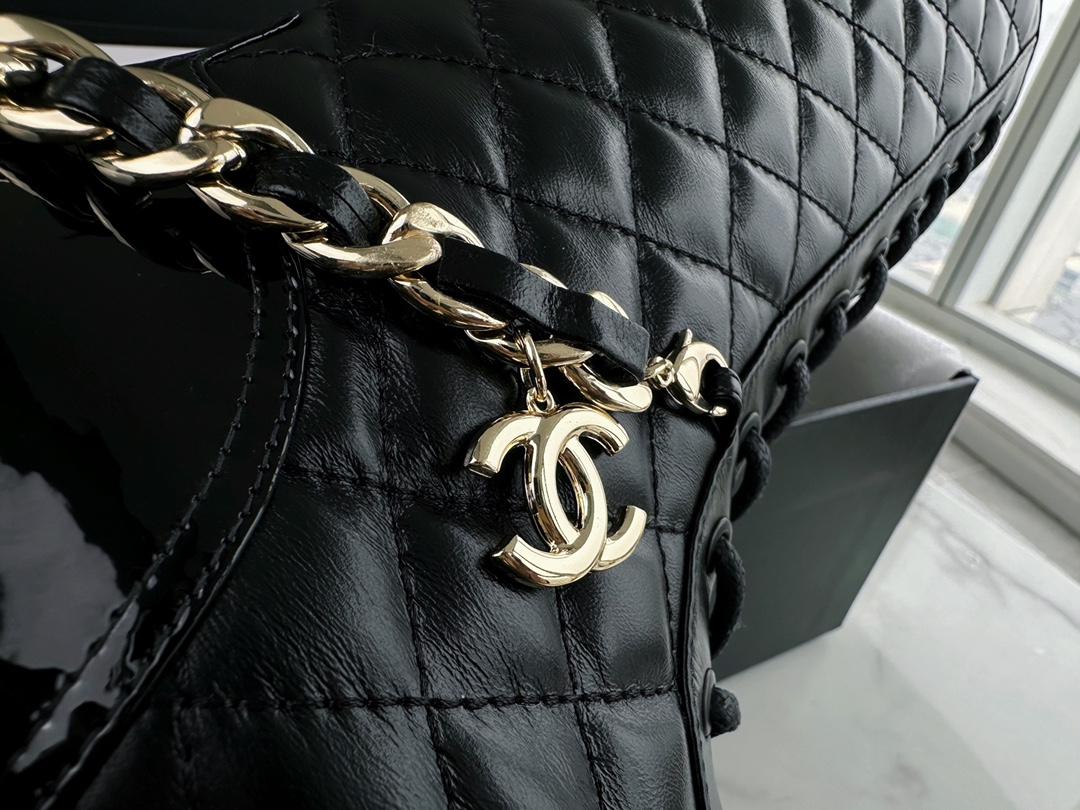 Chanel  23b  Chain Long Martin Boots: Crafted from black oil leather and black patent leather, with a leather combination sole. Classic diamond-pattern stitching and chain elements intertwine on the vamp