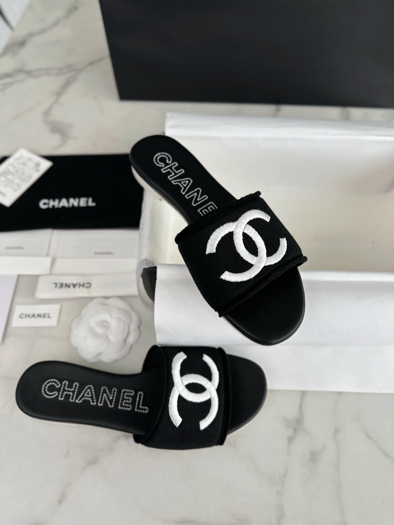 Chanel Black Double C Embroidered Slides: Featuring a Striking Black and White Color Block Design on the Upper, Karen Satin Fabric with Imported Thread Embroidery, Finished with a White Leather Sole. 